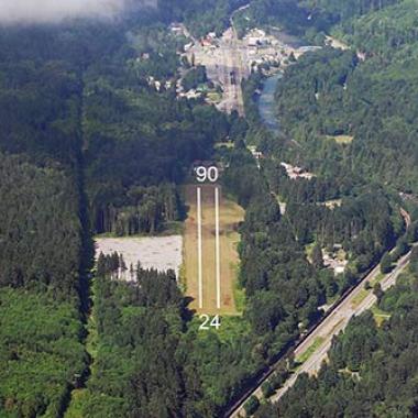 Skykomish Airport Runway located in the middle of large trees and a highway on the right.